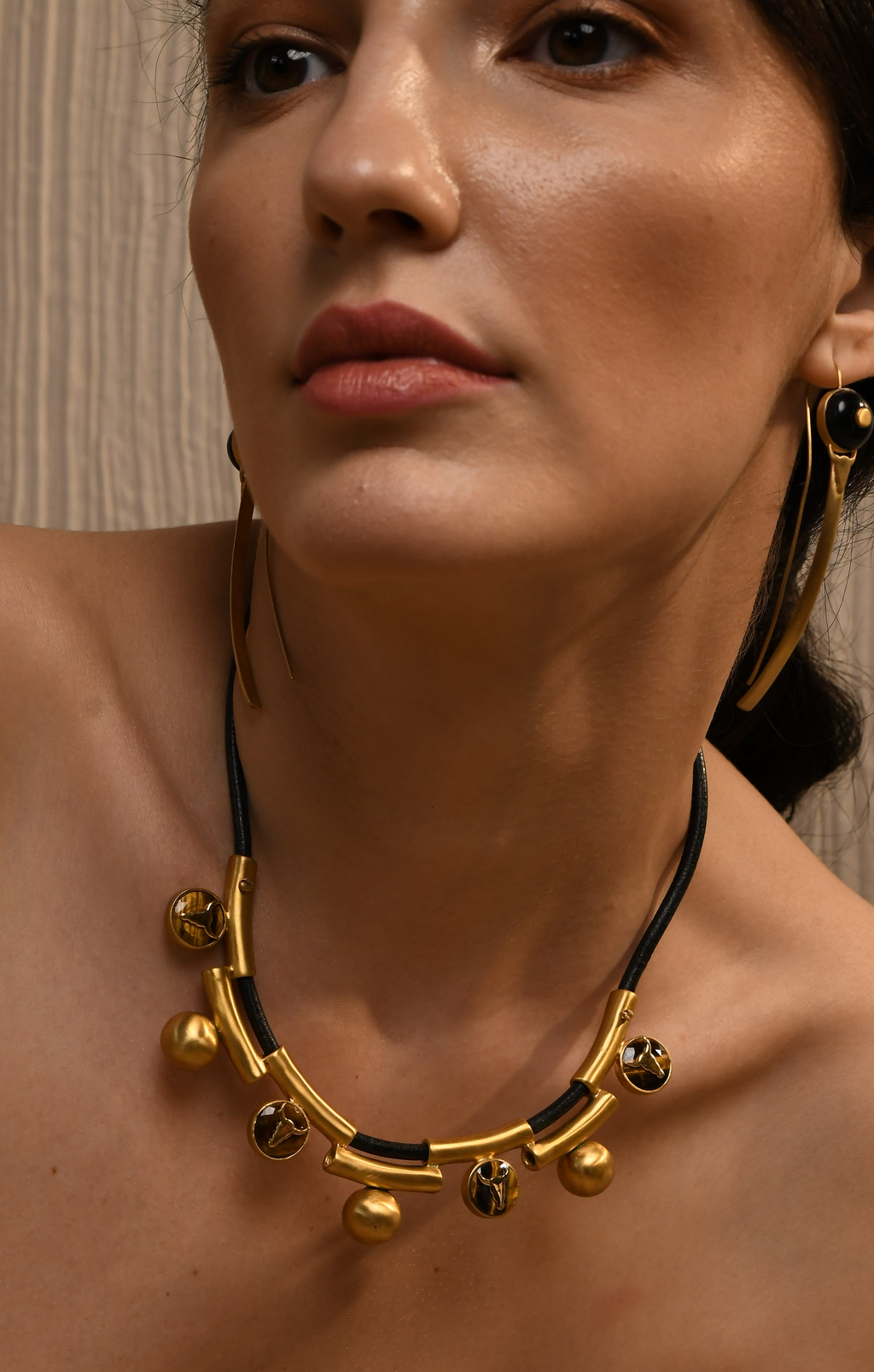 Woman wearing a gold and black necklace with hoop earrings.