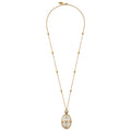 A gold chain necklace featuring a long drop pendant with a white enamel background and gold floral motifs, displayed against a solid white background.
